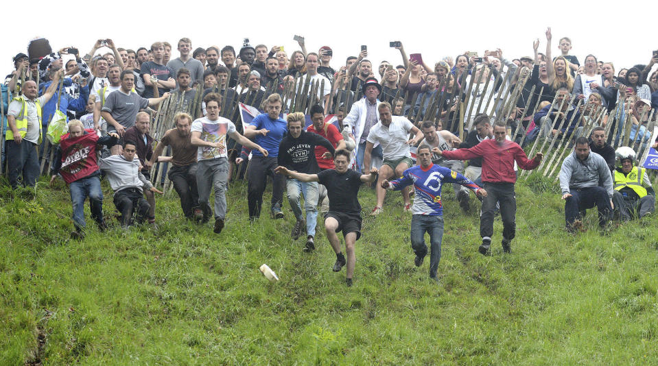 Competitors at the start of the annual unofficial cheese rolling at Cooper’s Hill in Brockworth, England, Monday May 29, 2017, where a cheese has been chased down the 200 yard, (183-metre) one-in-three gradient hill, annually, since the early 1800’s. A 9-lb round Double Gloucester cheese is set in motion at the top of the hill an the competitors chase after it – the first person to cross the finish line at the bottom of the hill wins the cheese. (Ben Birchall/PA via AP)