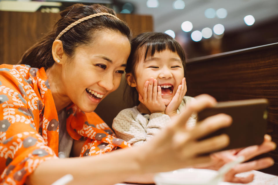 Pretty young mom taking selfies with lovely little girl in the restaurant joyfully.