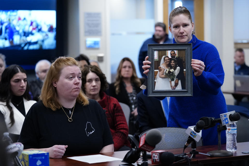 Elizabeth Seal holds a photo from Megan Vozzella's wedding to Steve Vozzella, Thursday, Feb. 1, 2024, in Augusta, Maine, during a hearing of the independent commission investigating the law enforcement response to the mass shooting in Lewiston, Maine. Megan Vozzella, seated at left, spoke about her life since her husband Steve was killed in the mass shooting. (AP Photo/Robert F. Bukaty)