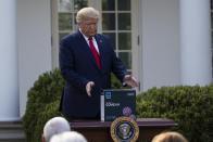 President Donald Trump reaches for a box containing a 5-minute test for COVID-19 from Abbott Laboratories, in the Rose Garden of the White House, Monday, March 30, 2020, in Washington. (AP Photo/Alex Brandon)