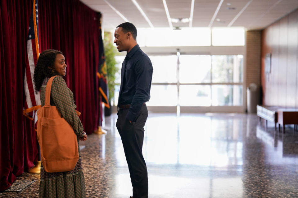 Two people having a friendly conversation in a hall with an American flag in the background