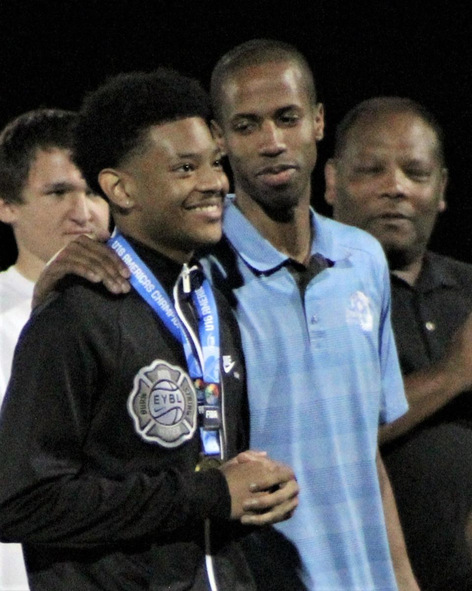 Bartlesville High School basketball player David Castillo, left, displays his USA Basketball 16U gold medal to the crowd at Custer Stadium during a football halftime last September. Bartlesville head basketball coach Clent Stewart , center, and dad Nate Castillo look on.