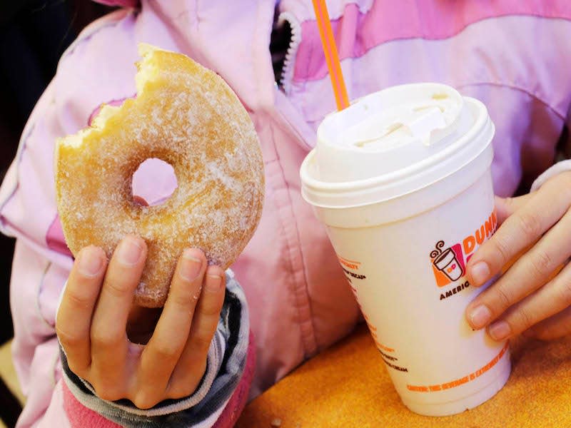 a person holding dunkin donuts coffee cup and donut