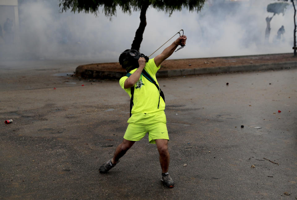 A protester fires a slingshot towards riot policemen, during a protest against deteriorating living conditions and strict coronavirus lockdown measures, in Tripoli, north Lebanon, Thursday, Jan. 28, 2021. Violent confrontations for three straight days between protesters and security forces in northern Lebanon left a 30-year-old man dead and more than 220 people injured, the state news agency said Thursday. (AP Photo/Hussein Malla)