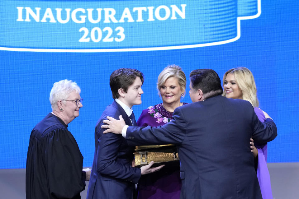 Illinois Gov. J.B. Pritzker, right, hugs his family, wife M.K. Pritzker, son Don, and daughter Teddi, after taking the oath of office from Mary Jane Theis, Illinois Supreme Court Chief Justice during ceremonies Monday, Jan. 9, 2023, in Springfield, Ill. (AP Photo/Charles Rex Arbogast)