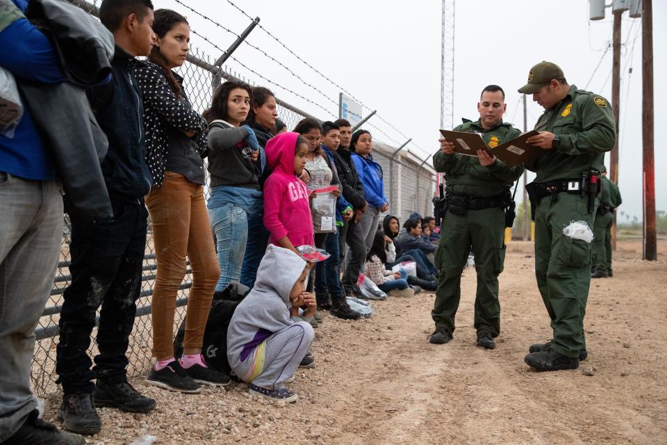 A large group of migrant families wait along the side of the road to be transported after turning themselves in to Border Patrol agents in Penitas, Texas, on Tuesday, Feb. 26, 2019.