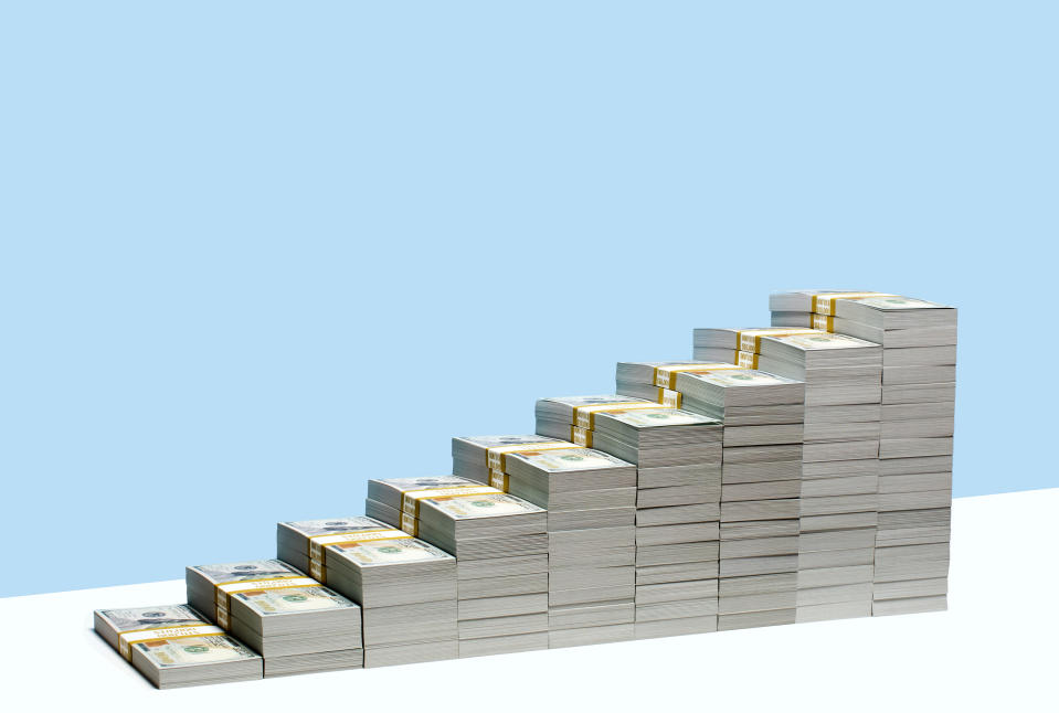 9 stacks of US $100 bill bundles in ascending size order on white shelf, blue background