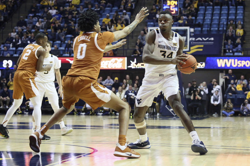 West Virginia forward Oscar Tshiebwe (34) goes to pass the ball as he is defended by Texas forward Gerald Liddell (0) during the second half of an NCAA college basketball game Monday, Jan. 20, 2020, in Morgantown, W.Va. (AP Photo/Kathleen Batten)
