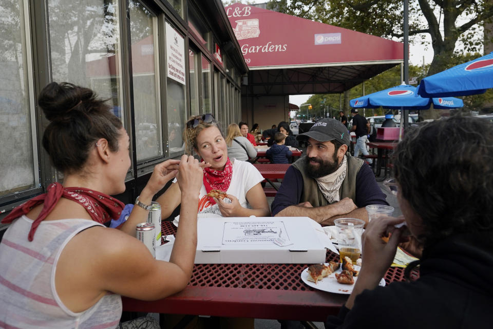 Nora Feher, Sarah Howard, Mike Sternfeld and Annie Simon, from left, share a pizza while eating outdoors, Sunday, Oct. 4, 2020, at L&B Spumoni Gardens in the Brooklyn borough of New York. Feher and Sternfeld both work in the food service industry. The restaurant is in a Zip Code that has seen a spike in coronavirus cases recently. On Sunday, New York's mayor said he asked the state for permission to close schools and reinstate restrictions on nonessential businesses in several neighborhoods because of a resurgence of virus cases. Should restrictions be imposed, the restaurant may have to close its outdoor dining area and restrict itself to takeout and delivery only. (AP Photo/Kathy Willens)