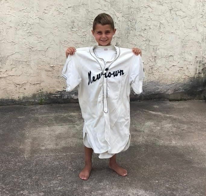 Six-year-old Tyler Neeld, now a starter on the Council Rock Newtown Little League team, holds up great grandfather Harry Neeld's Newtown jersey.