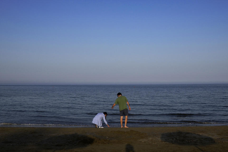 A couple of tourists enjoy the sea at Makenzi beach in southern coastal city of Larnaca, Cyprus, Monday, May 30, 2022. Hundreds of Russian and Ukrainian Orthodox faithful visiting Cyprus would stream daily past the icon of the Virgin Mary at Kykkos Monastery to venerate the relic that tradition dictates was fashioned by Luke the Evangelist and blessed by the Virgin herself. But a European Union ban on flights to and from Russia as a result of Russia's invasion of Ukraine has meant a loss of 800,000 vacationers - a fifth of all tourists to Cyprus in record-setting 2019. (AP Photo/Petros Karadjias)