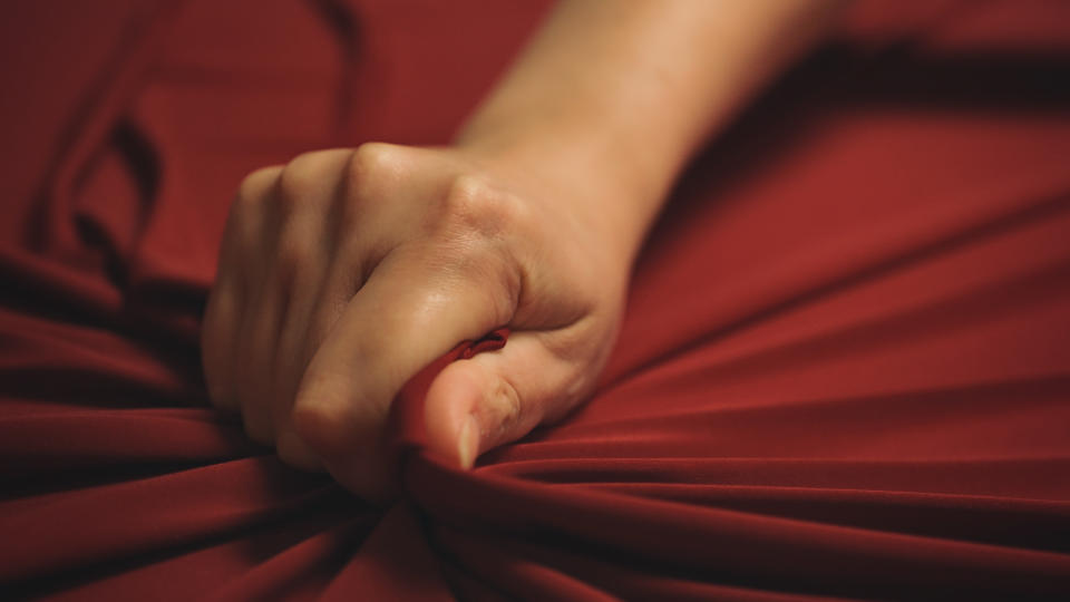 A clenched hand tightly grasps red fabric, creating tension and wrinkles