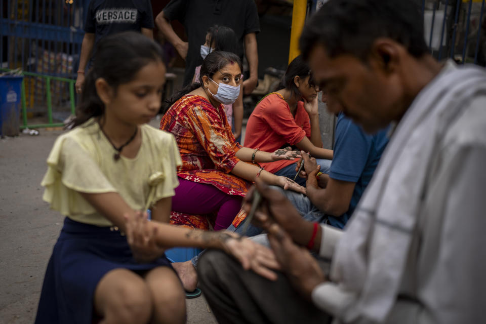 A woman wearing a mask as a precaution against coronavirus gets her hands decorated with henna on the eve of the Hindu festival of Raksha Bandhan in New Delhi, India, Thursday, Aug. 11, 2022. The Indian capital reintroduced public mask mandates on Thursday as COVID-19 cases continue to rise across the country. (AP Photo/Altaf Qadri)