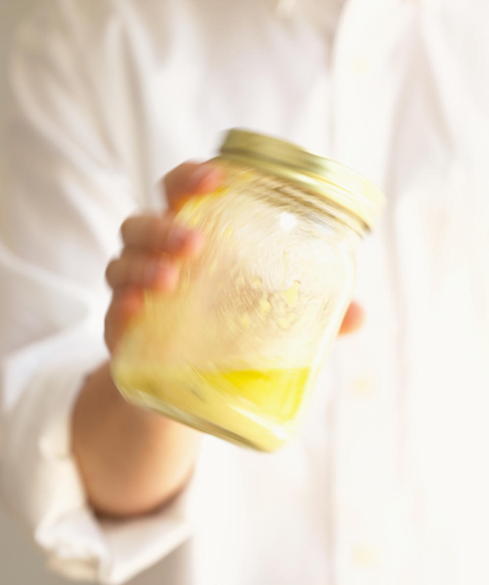 A person in a white shirt shaking a glass jar with mayonnaise