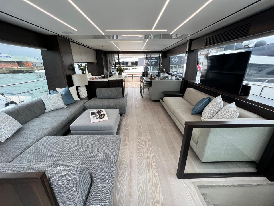 The main deck interior of a Sunseeker 76 yacht viewed from the front, with the living area's large couches in the foreground