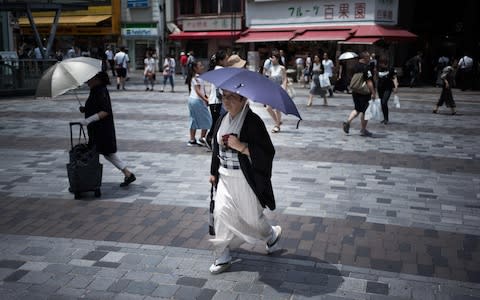 A woman shelters herself from the sun as she walks along a street in Tokyo - Credit: MARTIN BUREAU/AFP/Getty Images