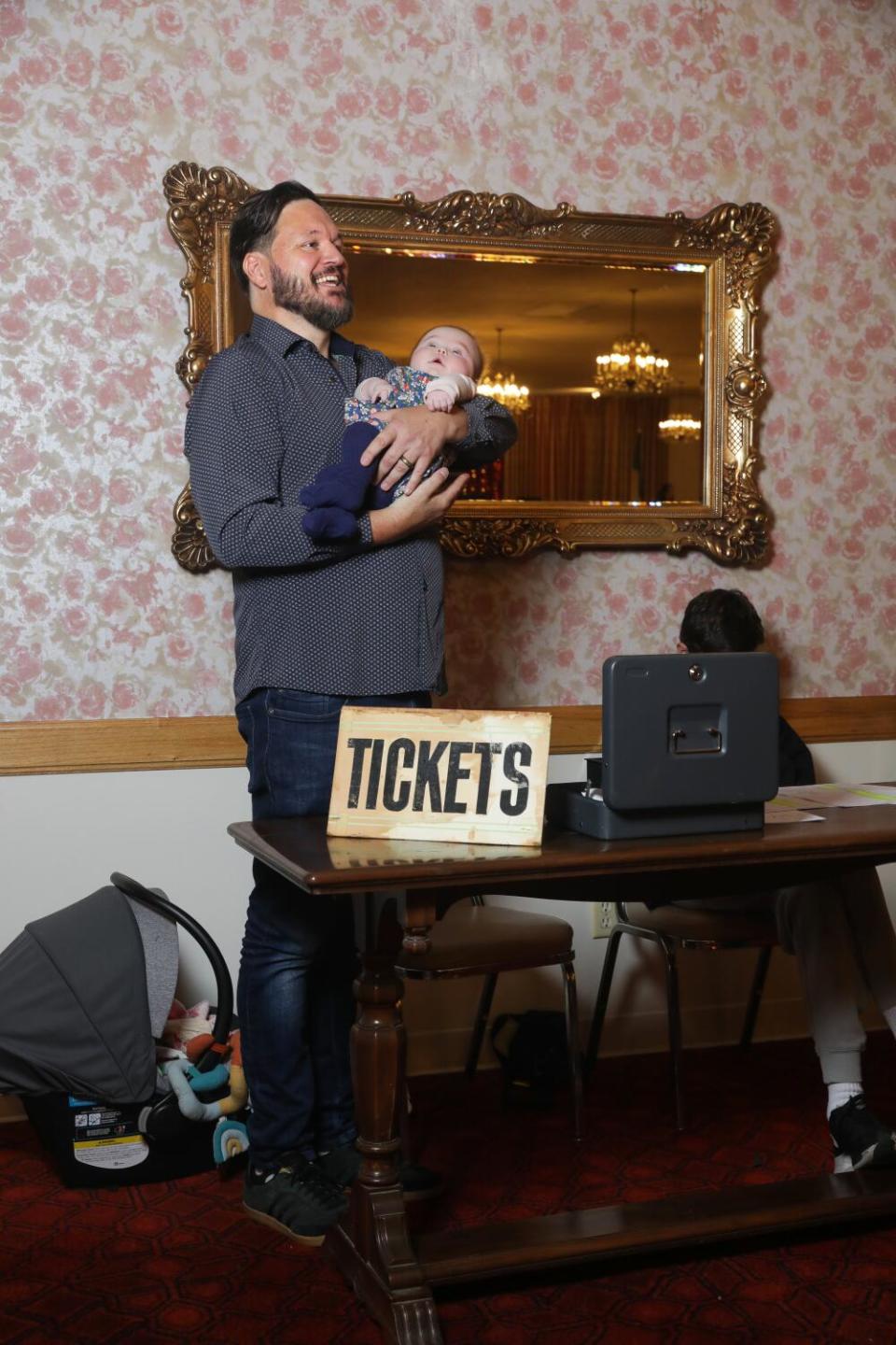 A man holds his baby behind a table with a sign that says "tickets" at the Garibaldina Society.