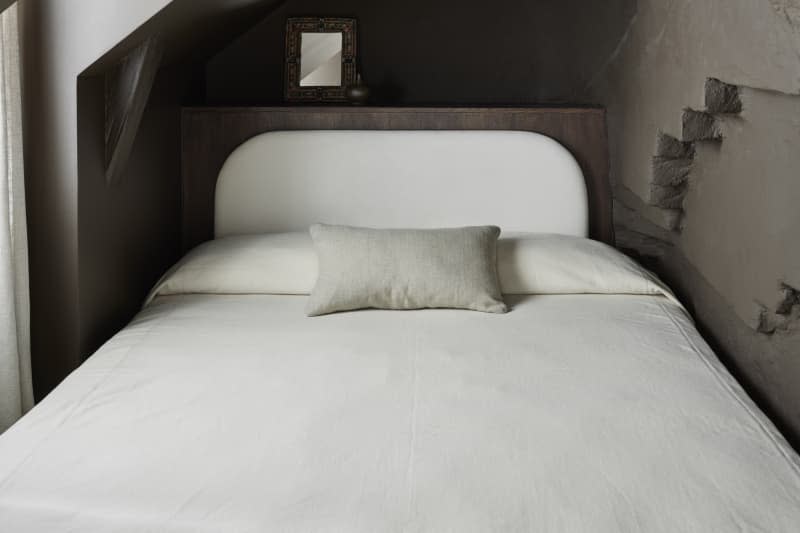 low white linen bed with gray painted exposed brick cut outs in small nook