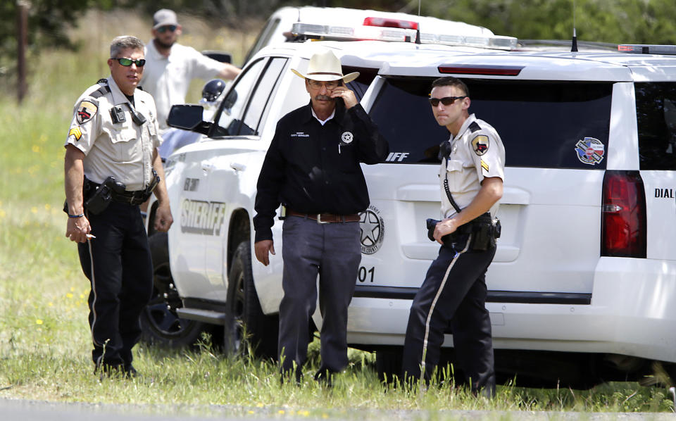 Kerr County Sheriff Rusty Hierholzer, center, makes a phone call, Monday, April 22, 2019, where his deputies guard the entrance to a private road near Kerrville, Texas, where a twin-engine Beechcraft airplane crashed earlier in the day, killing all six people on board. (Bob Owen/The San Antonio Express-News via AP)