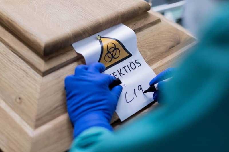 A funeral director writes "C19" on a sign saying "Infectious" on a coffin containing a deceased person who died from Covid-19.In 2021, the respiratory disease was the second most common cause of death worldwide, according to a new study. Rolf Vennenbernd/dpa