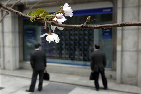 Two businessmen look at an electronic stock quotation board, as cherry blossoms bloom, outside a brokerage in Tokyo April 9, 2014. REUTERS/Issei Kato