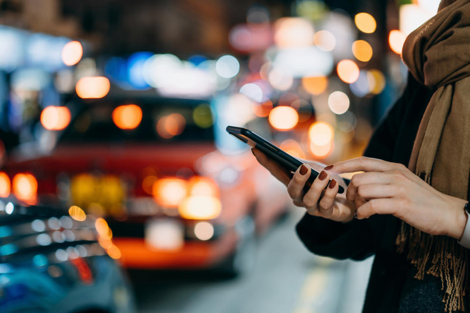 A woman with red nails on her phone at night by a line of cars