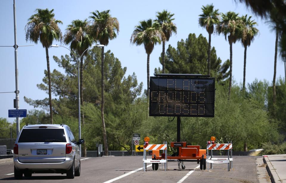 A vehicle drives past a temporary sign set up at an entrance at Kiwanis Park lets patrons know what is closed as new rules have shut down many activities due to the surge in coronavirus cases Tuesday, June 30, 2020, in Tempe, Ariz. (AP Photo/Ross D. Franklin)