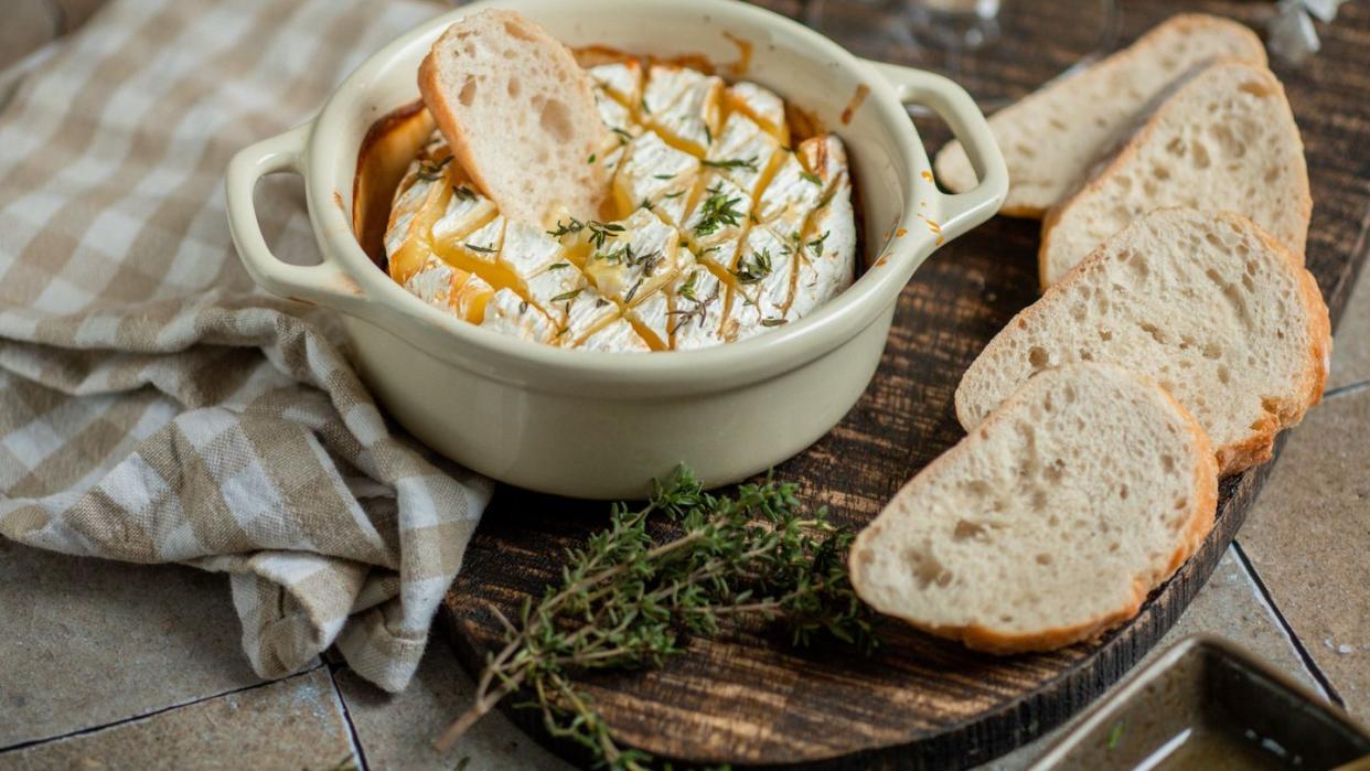 baked brie cheese with thyme herbs, honey and white wine in rustic kitchen with baguette bread