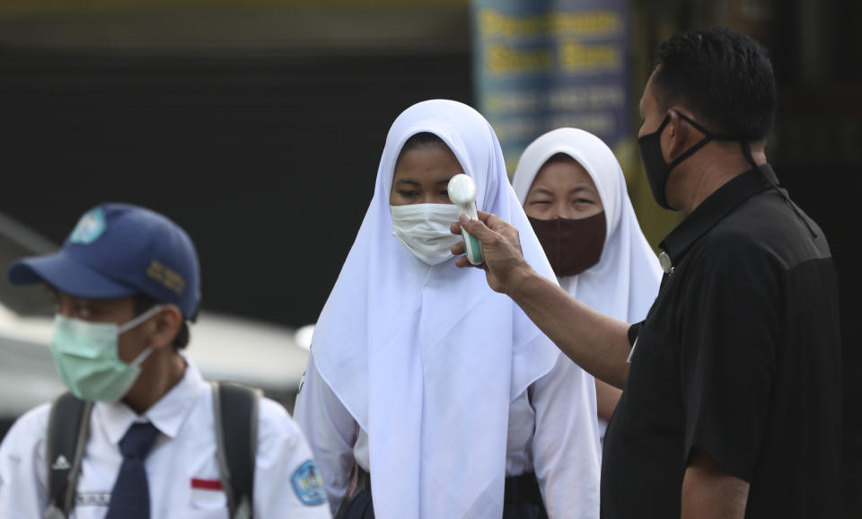 A security guard checks the body temperature of a student before entering a school amid coronavirus outbreak during the first day of school reopening at a state high school in Bekasi on the outskirts of Jakarta, Indonesia July 13, 2020. (AP Photo/Achmad Ibrahim)