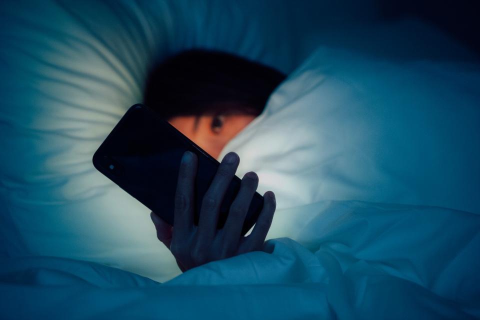 A woman hiding under the blanket and using phone late at night on her bed