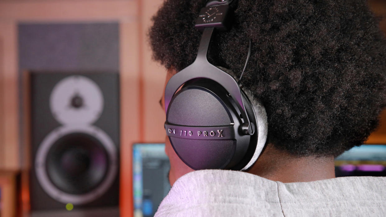  Beyerdynamic DT 770 Pro X Limited edition worn by a man, facing away from the camera, with bookshelf speakers in the background. 