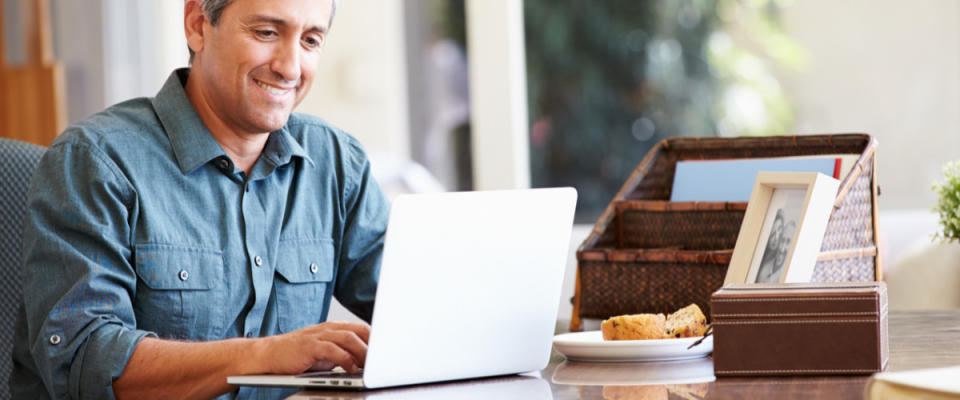 Mature Hispanic Man Using Laptop On Desk At Home