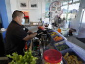 Barman Gustavo prepares drinks behind plexiglass protective wall at Maria Sol on the Santa Monica Pier as the pier restaurant opens for indoors service in Santa Monica, Calif., Wednesday, March 31, 2021. Los Angeles County can reopen even more businesses while expanding how many people are allowed to dine indoors or catch a movie, California public health officials announced Tuesday, March 30, 2021. The county of 10 million people was one of several that moved into the state's orange tier, which is the second-least restrictive of California's four-tier system. (AP Photo/Damian Dovarganes)