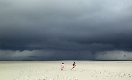 Jack Segar (R) and Finn Harden run across a deserted sandbar beach outside Barnstable Harbor as storm clouds associated with Tropical Storm Arthur pass over Cape Cod Bay behind them in Barnstable, Massachusetts, July 4, 2014. REUTERS/Mike Segar