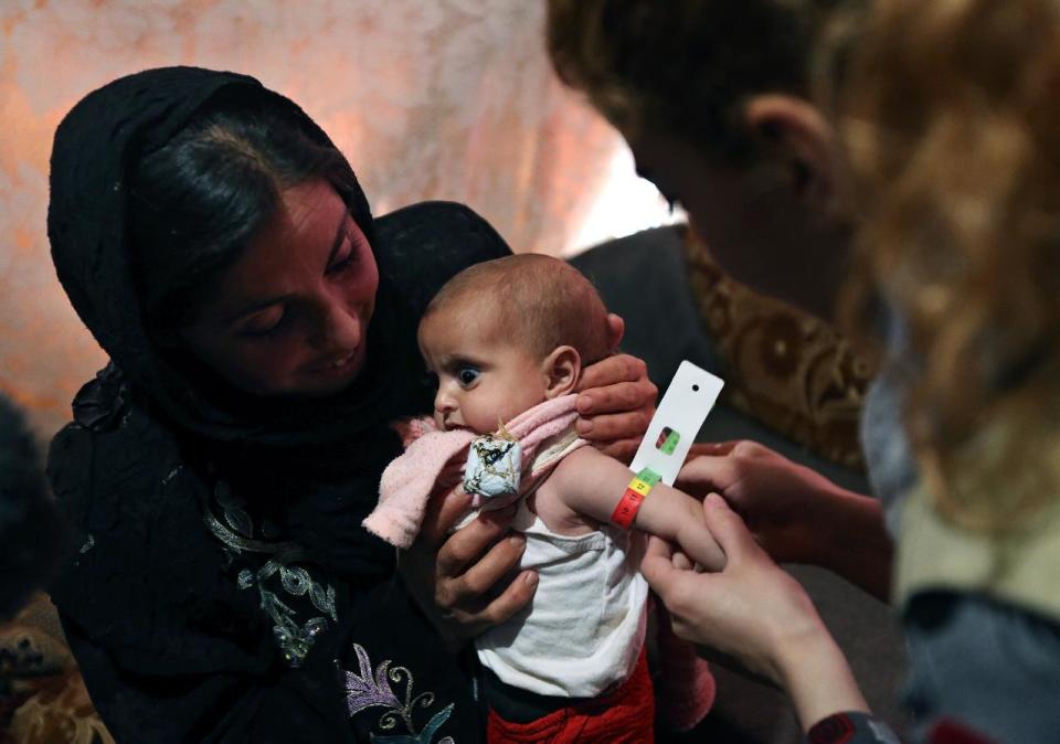 In this Tuesday, March 11, 2014 photo, an aid worker measures the upper arm circumference of 9-month-old Shurouk as her mother Mervat, 31, holds her inside their tent at a camp for Syrian refugees camp in Kab Elias, in Lebanon's Bekaa Valley. The measurement is an immediate indicator of malnourishment. Trapped in her northern Syrian village by fighting, Mervat watched her newborn baby progressively shrink. Her daughter’s dark eyes seemed to grow bigger as her face grew more skeletal. Finally, Mervat escaped to neighboring Lebanon, and a nurse told her the girl was starving. Such stark malnutrition was rare in Syria in the past, but as the country’s conflict enters its fourth year, international aid workers fear malnutrition is rising among children in Syria and among refugees amid the collapse in the health care system.(AP Photo/Bilal Hussein)