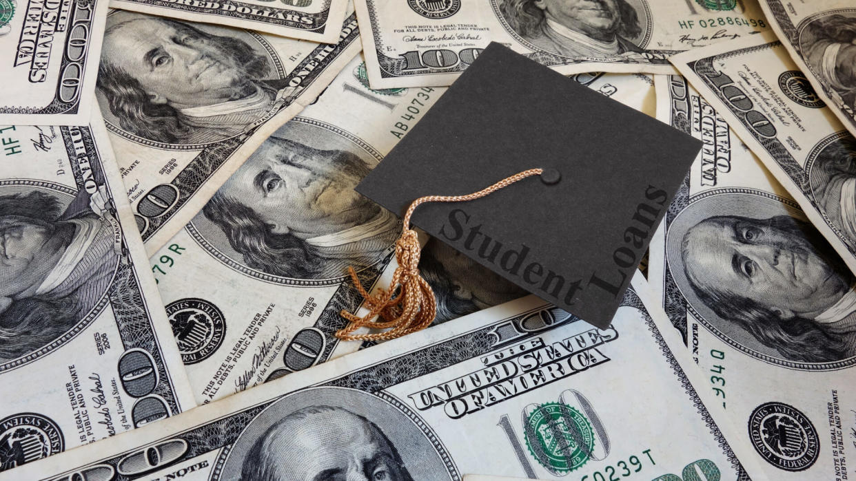 Miniature graduation cap with Student Loans text, on assorted cash.