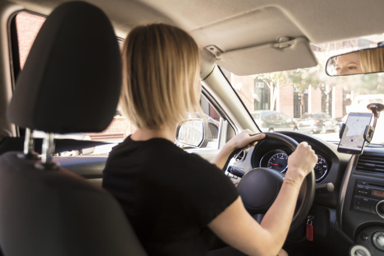 View from passenger in back seat of beautiful young blond woman driver, chauffeur driving a car with directions on her phone on a beautiful sunny day, Commute to work or to airport