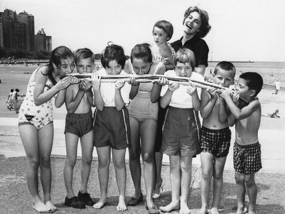 Eight children share a large hot dog during National Hot Dog Month at Oak Street Beach in Chicago, 1959.