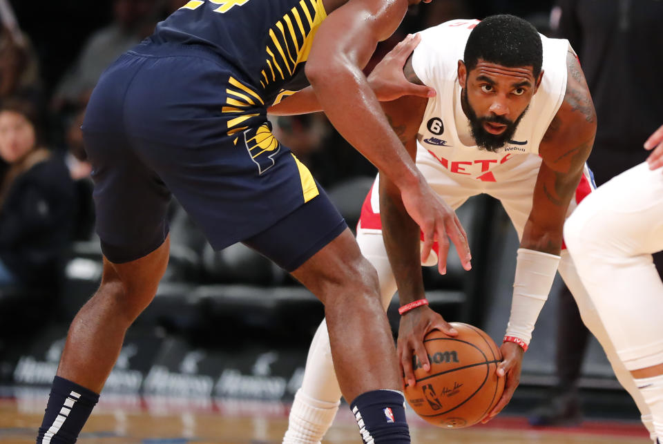 Brooklyn Nets guard Kyrie Irving looks for help against Indiana Pacers guard Buddy Hield during the second half of an NBA basketball game, Saturday, Oct. 29, 2022, in New York. (AP Photo/Noah K. Murray)