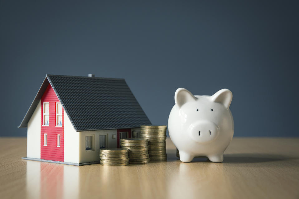 A miniature house, three stacks of coins, and a piggy bank.