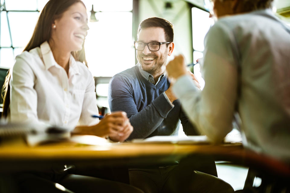 Young happy couple communicating with their financial advisor on a meeting in the office. Focus is on man.