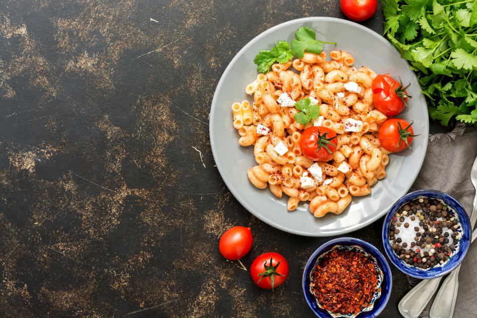 Pasta with feta cheese, sauce and baked tomatoes. Italian dish. Dark background, flat lay