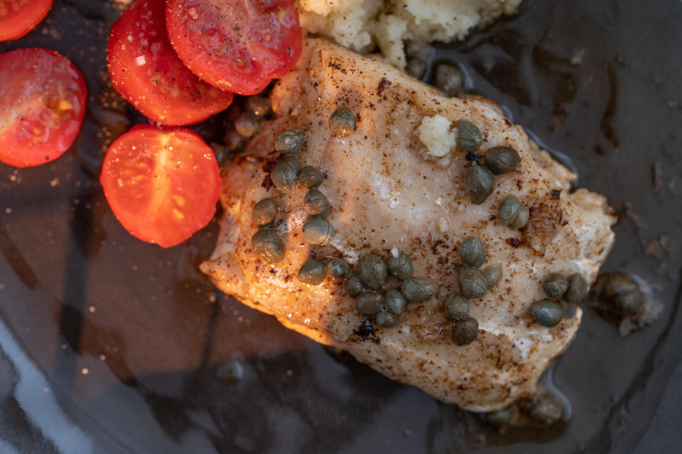 A piece of cod with fried capers and roasted tomatoes.