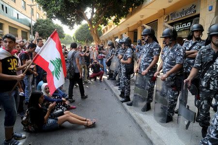 Protestors carry a Lebanese flag in front of riot police at one of the entrances to the environment ministry in downtown Beirut, Lebanon September 1, 2015. REUTERS/Aziz Taher