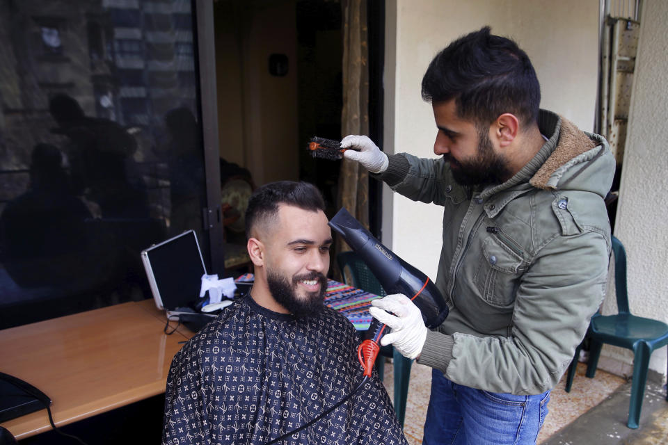 Barber Fouad Lalo cuts hair on the balcony of a customer's home, in Beirut, Lebanon, Thursday, March 26, 2020. Lebanon has been under a government-ordered lockdown since last week in an effort to stem the spread of the coronavirus. (AP Photo/Bilal Hussein)