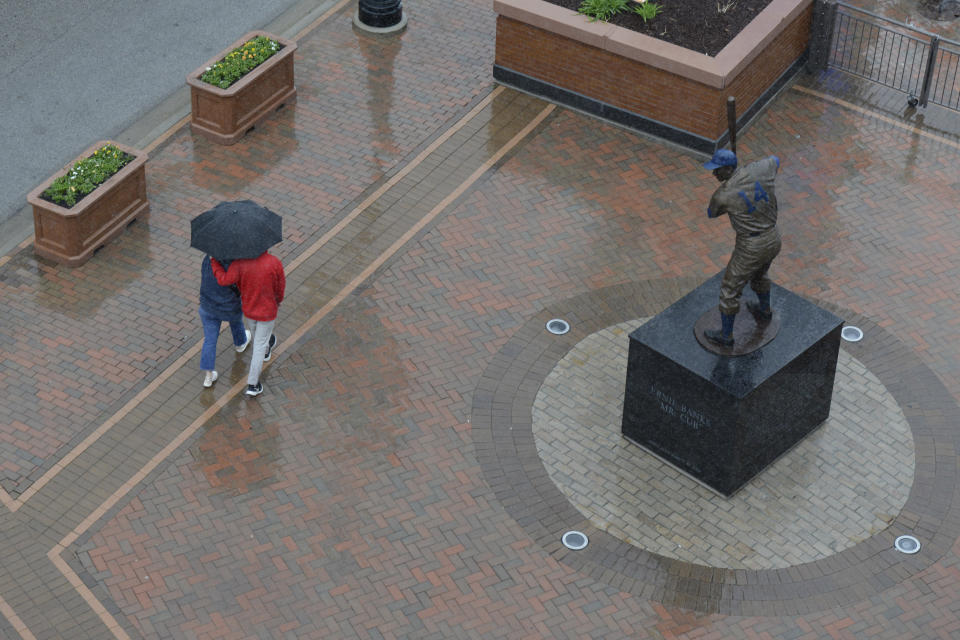 A couple walks in the rain near a statue of Chicago Cubs Hall of Fame player Ernie Banks during a rain delay before a baseball game between the Chicago Cubs and Pittsburgh Pirates at Wrigley Field, Sunday, April 24, 2022, in Chicago. (AP Photo/Paul Beaty)