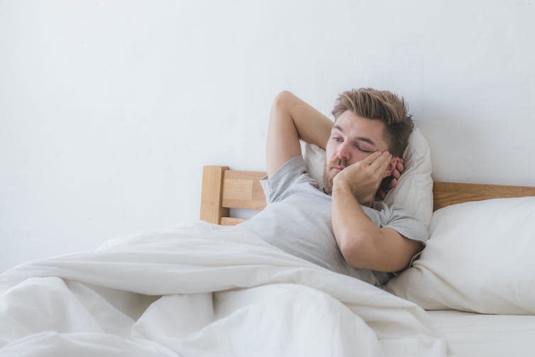 Hungover man lays in bed looking tired and depressed.