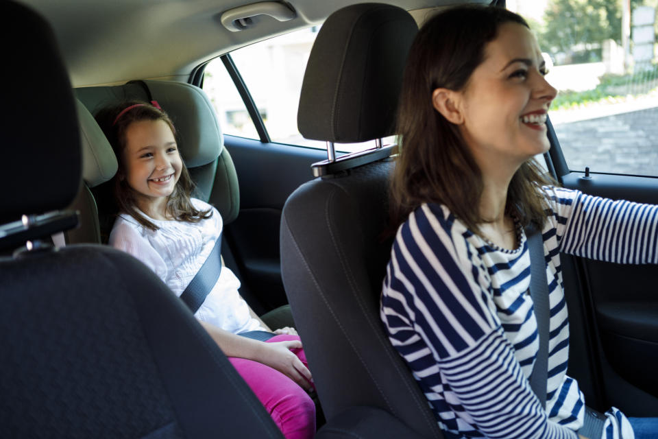 Mom driving a car smiling at her daughter sitting in the backseat with a seatbelt on, both look happy
