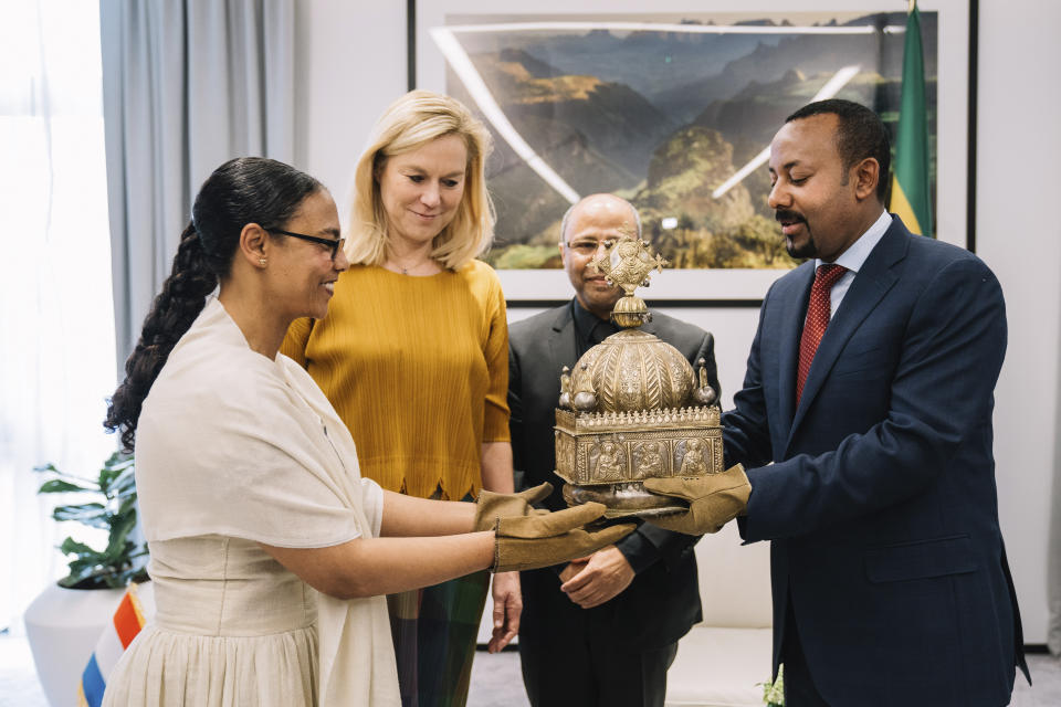 Ethiopia's Prime Minister, Abiy Ahmed, right, receives with gloved hands during a ceremony to hand over a lost crown Thursday, Feb. 20, 2020. The 18th Century Ethiopian crown has been returned home after being hidden in a Dutch flat for the past 21-years. (The Office of Prime Minister Abiy Ahmed via AP)