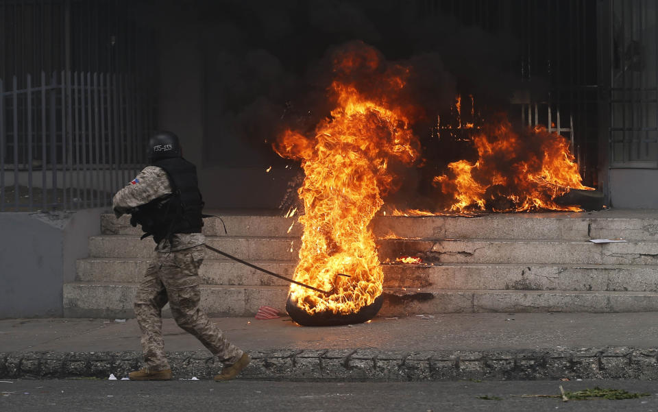 A National police officer removes a burning tire from a government building that was set by anti-government protesters demanding the resignation of President Jovenel Moise in Port-au-Prince, Haiti, Sunday, June 9, 2019. The protesters are demanding further investigation into the fate of funds that resulted from subsidized oil shipments from Venezuela. (AP Photo/Dieu Nalio Chery)